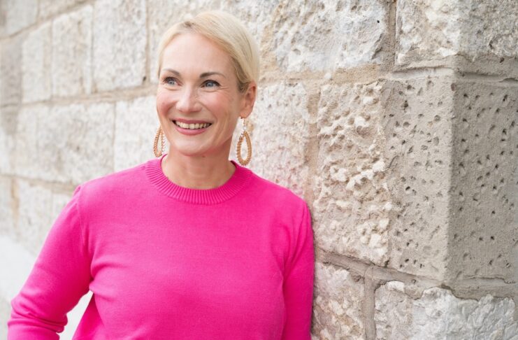 Sichtbarkeit Anke Ames angelent an einer Steinwand in einem Pinkfarbenen Oberteil! Foto©Schmelz Fotodesign Anke Ames
